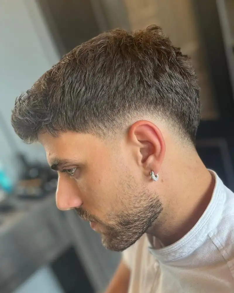 Chico con un corte de pelo moderno, un pendiente y barba arreglada. High fade.